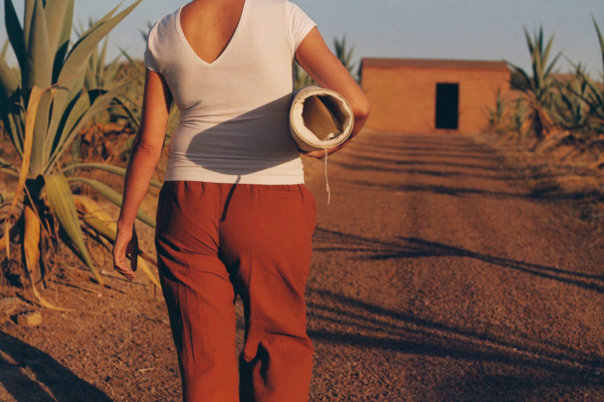 Una mujer camina hacia un taller de adobe cargando un lienzo enrollado